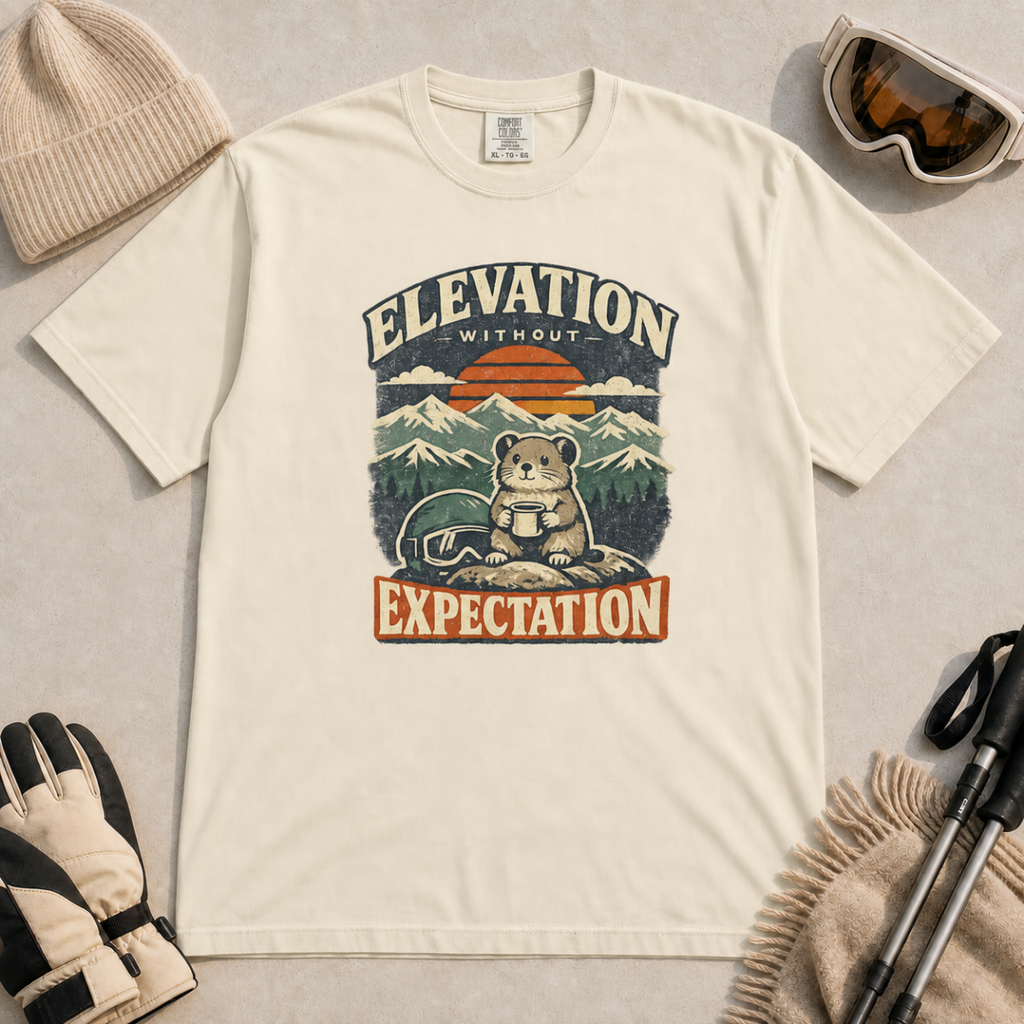 Ivory white t-shirt featuring a mountain rodent with a mug and ski goggles beneath retro sunset scenery and the phrase “Elevation Without Expectation.”
