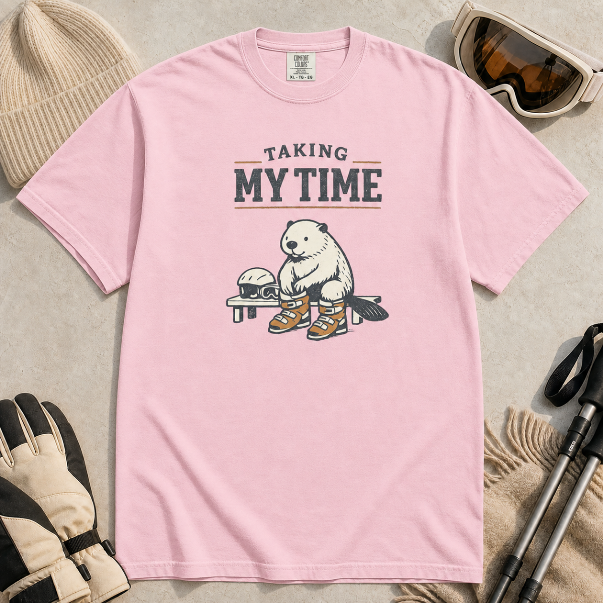Blossom pink t-shirt featuring a beaver seated on a bench fastening snowboard boots beneath “Taking My Time” text.