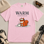 Blossom pink t-shirt featuring a bundled-up squirrel warming its paws beside a steaming mug under “Warm Eventually” text.
