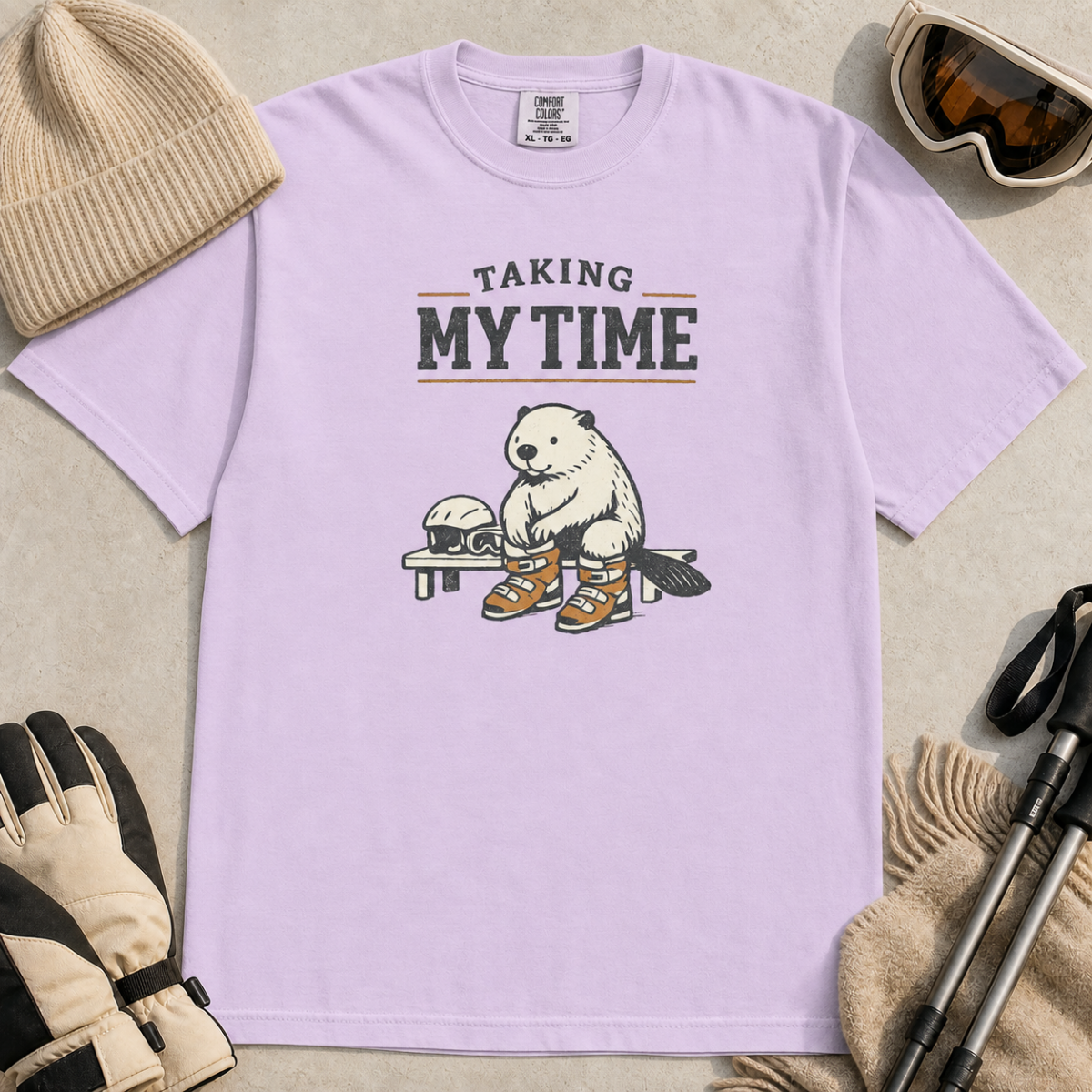 Orchid purple t-shirt featuring a beaver seated on a bench fastening snowboard boots beneath “Taking My Time” text.