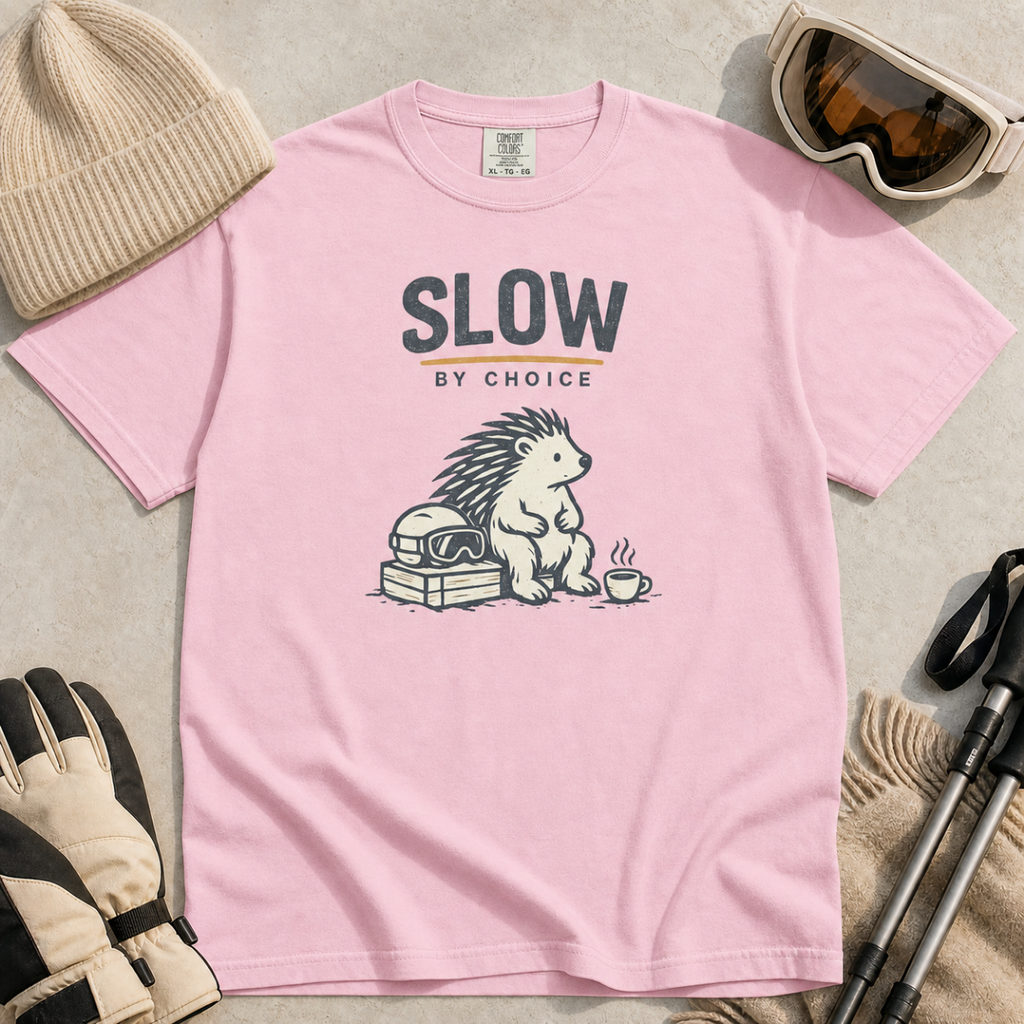 Blossom pink t-shirt featuring a seated hedgehog beside ski goggles and a hot drink beneath “Slow by Choice” text.