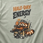 Close-up of a bay green t-shirt featuring a sleepy red panda lounging in a chair with the phrase “Half-Day Energy.”