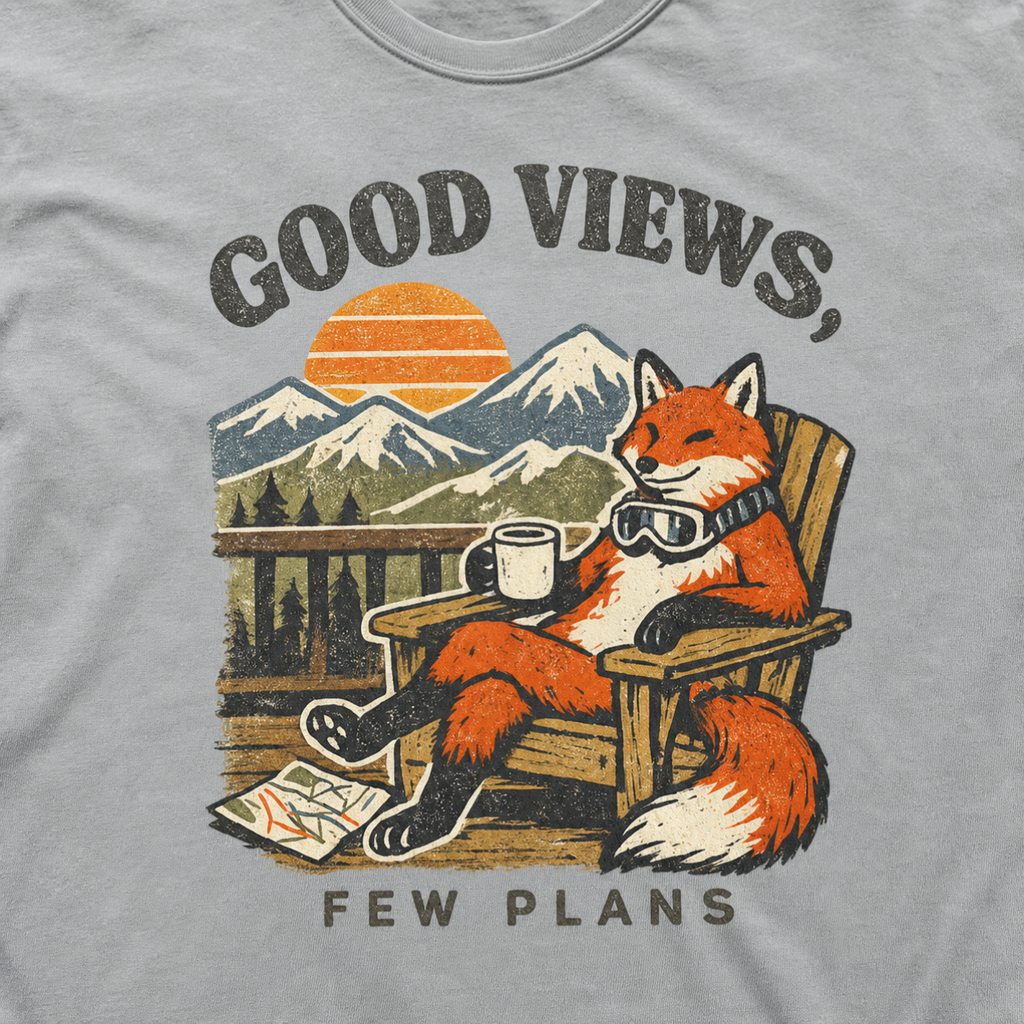 Close-up of a granite gray t-shirt design showing a fox relaxing with a mug before mountain scenery and the phrase “Good Views, Few Plans.”
