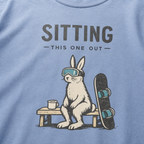 Close-up of a rabbit in ski goggles sitting beside a mug and snowboard beneath “Sitting This One Out” lettering.