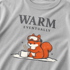 Close-up of a granite gray t-shirt design showing a ski-goggle-wearing squirrel beside a hot drink under “Warm Eventually” text.