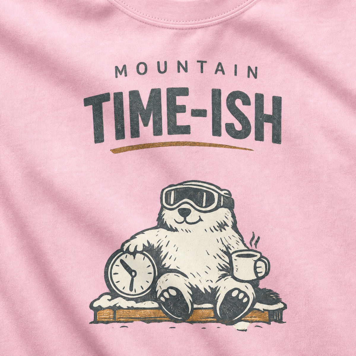 Close-up of a blossom pink t-shirt design showing a relaxed marmot with ski goggles, a clock and steaming mug beneath the words “Mountain Time-ish.”