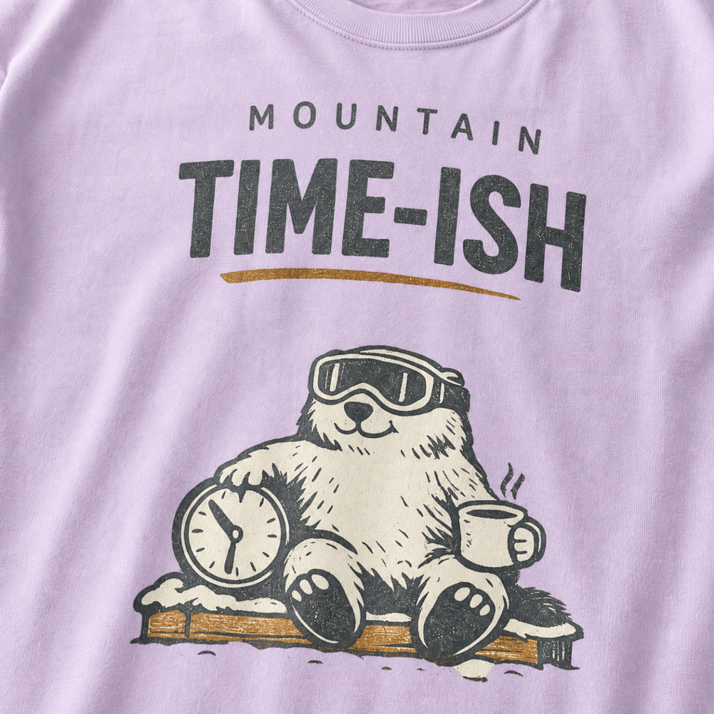 Close-up of an orchid purple t-shirt design showing a relaxed marmot with ski goggles, a clock and steaming mug beneath the words “Mountain Time-ish.”