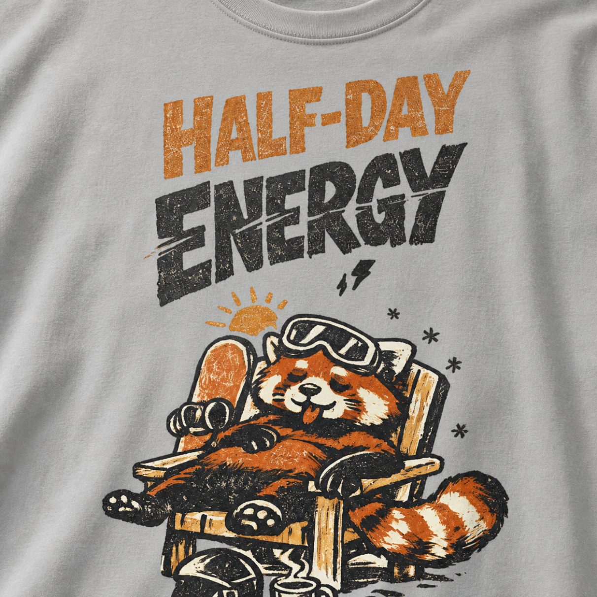 Close-up of a granite gray t-shirt featuring a sleepy red panda lounging in a chair with the phrase “Half-Day Energy.”