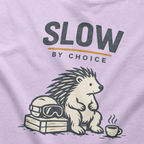 Close-up of a seated hedgehog resting beside ski goggles and a steaming mug under “Slow by Choice” lettering.