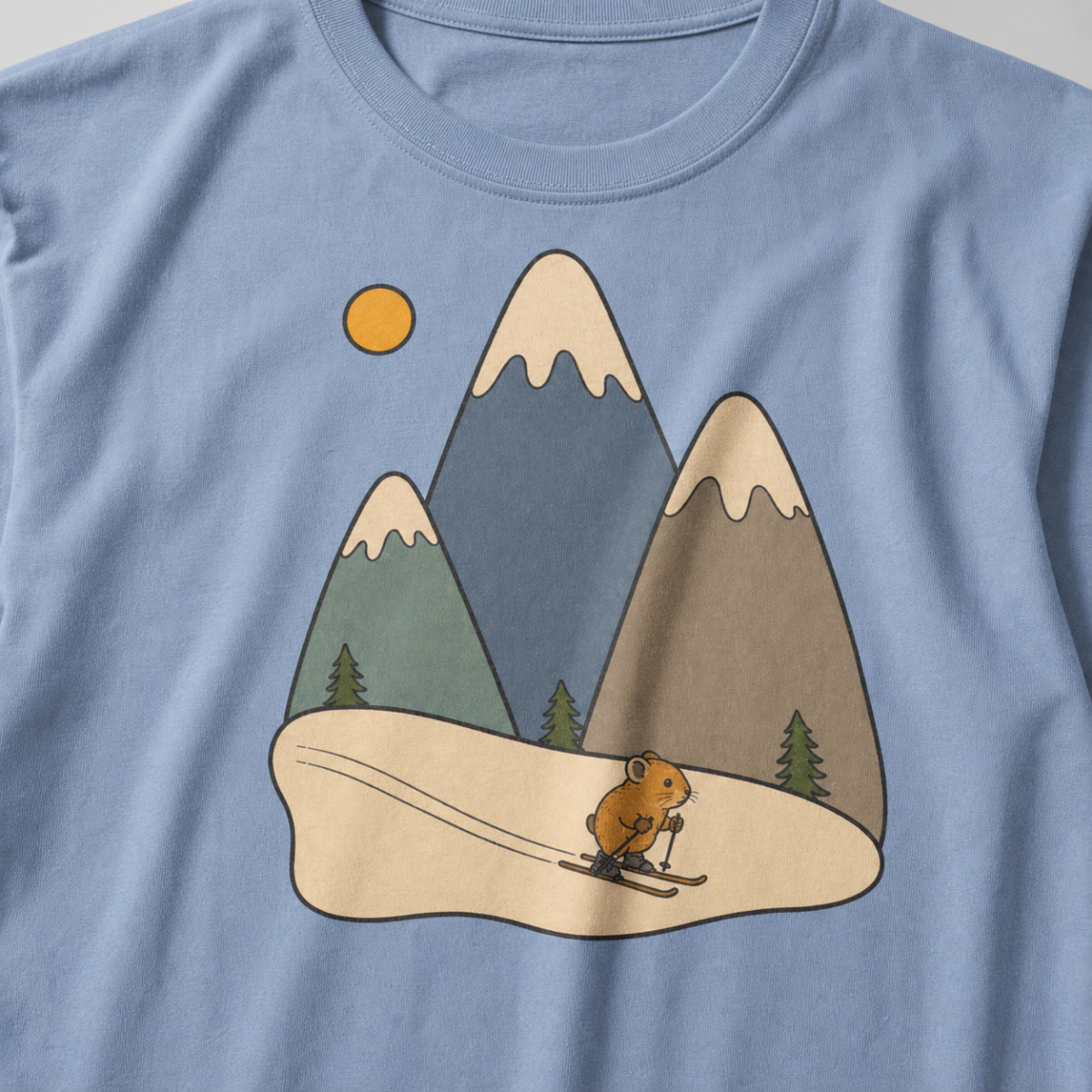 Close-up of a granite gray t-shirt featuring three muted snow-capped mountains, pine trees, a golden sun and a tiny animal skiing downhill.