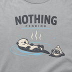 Close-up of a granite gray t-shirt featuring a relaxed otter floating in a hot spring beside ski goggles and a beanie, with the words “Nothing Pending.”