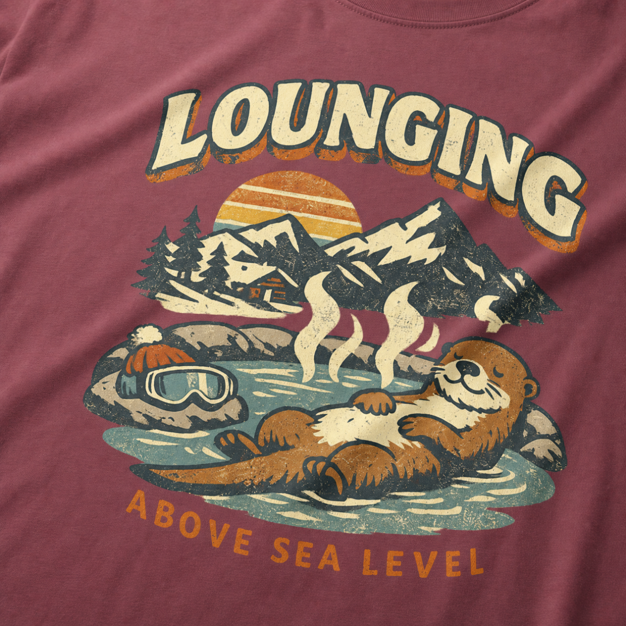 Close-up of a vintage otter hot spring design with snowy mountains, a sunset and the words “Lounging Above Sea Level.”