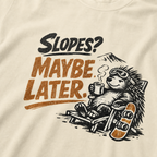 Close-up of a reclining hedgehog holding a hot drink beside a snowboard with “Slopes? Maybe Later.” lettering.
