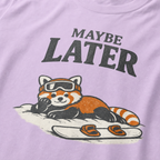 Close-up of an orchid purple t-shirt design featuring a red panda resting in the snow beside a snowboard beneath the words “Maybe Later.”