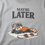 Close-up of a granite gray t-shirt design featuring a red panda resting in the snow beside a snowboard beneath the words “Maybe Later.”
