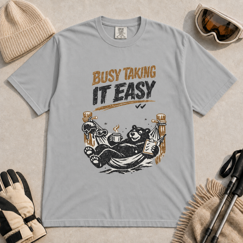 Granite grey t-shirt featuring a black bear resting in a hammock with ski gear and the words “Busy Taking It Easy.”