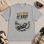 Granite grey t-shirt featuring a black bear resting in a hammock with ski gear and the words “Busy Taking It Easy.”