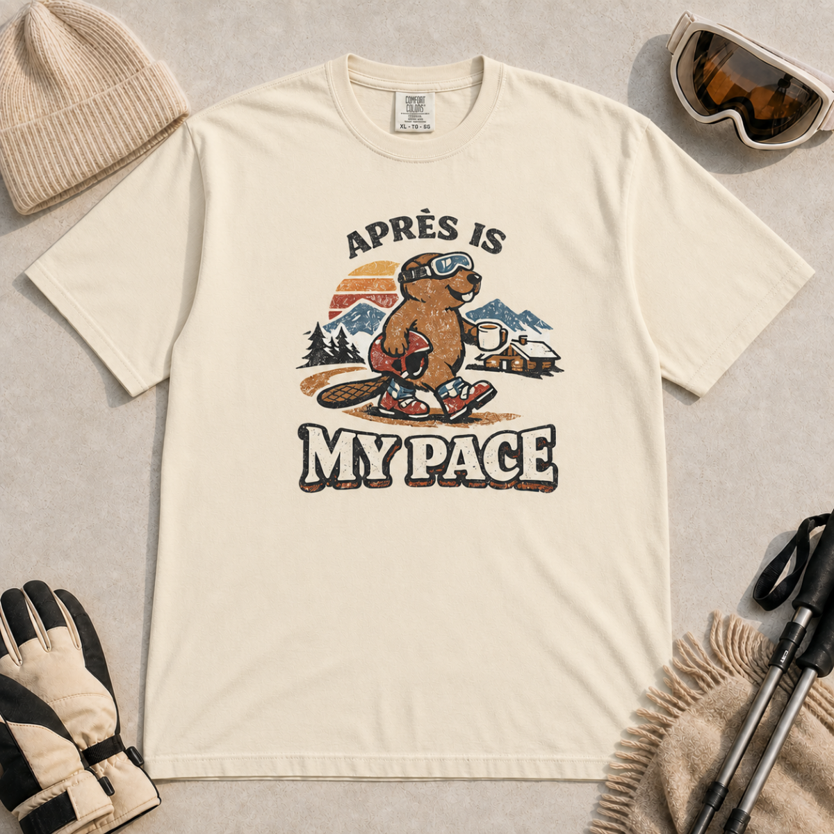 Ivory white t-shirt featuring a beaver in ski boots holding a mug beneath the words “Après Is My Pace.”