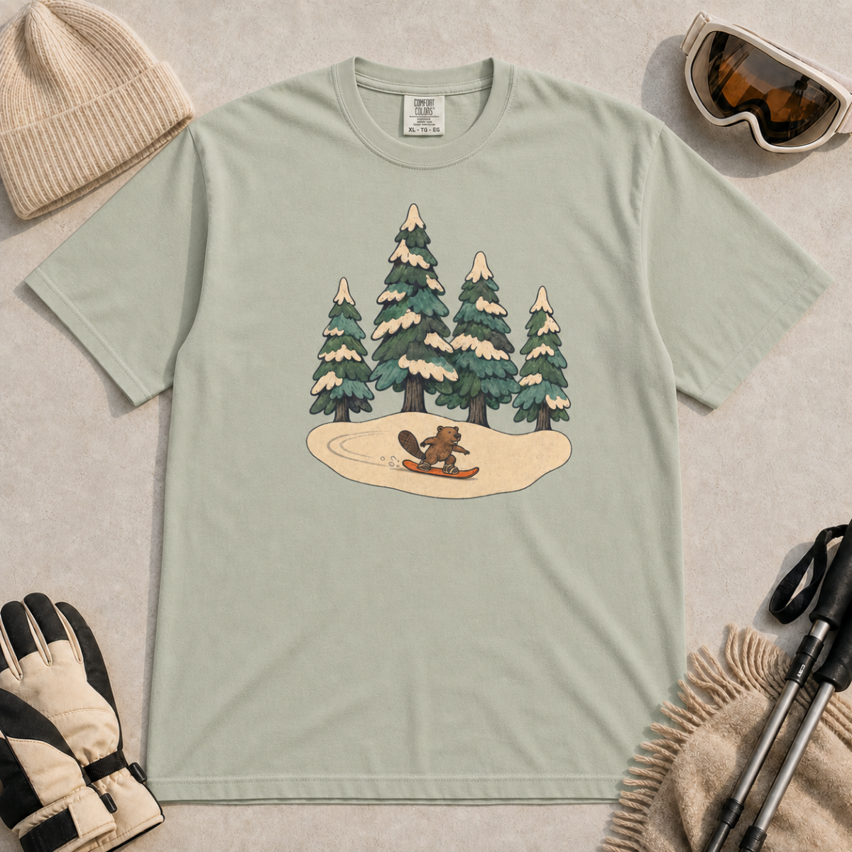 Bay green t-shirt featuring a small beaver snowboarding beneath four snow-covered pine trees.