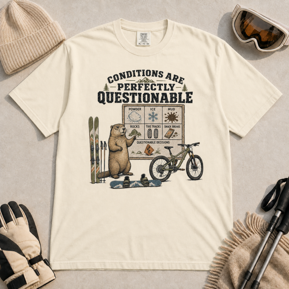 Ivory white t-shirt featuring a marmot with skiing, snowboarding, and mountain biking gear under “Conditions Are Perfectly Questionable” text.