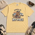 Butter yellow t-shirt featuring a beaver in ski boots holding a mug beneath the words “Après Is My Pace.”
