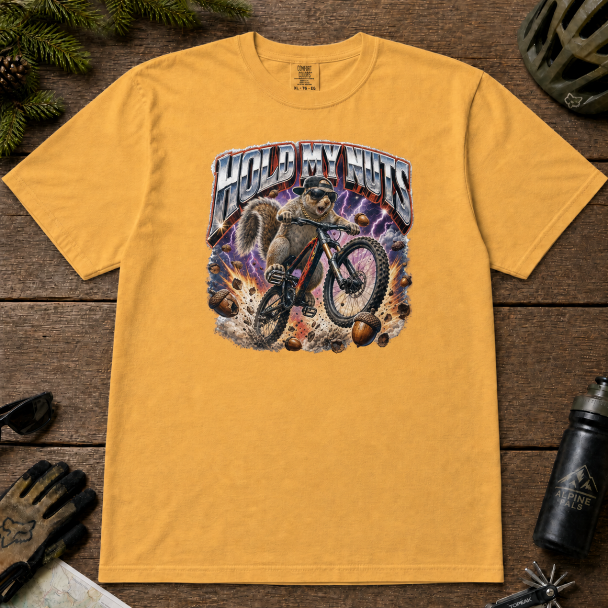 Mustard yellow t-shirt featuring a squirrel mountain biking through flying acorns beneath the words “Hold My Nuts.”