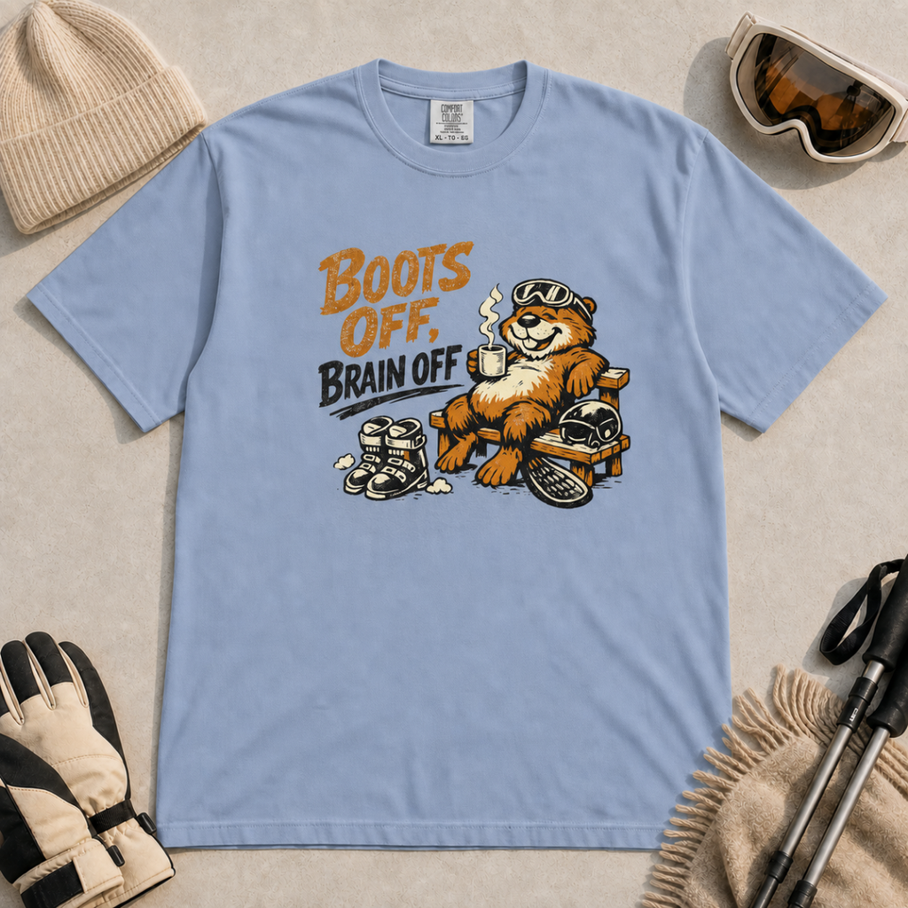 Washed denim blue t-shirt featuring a marmot relaxing on a bench with ski gear and the words “Boots Off, Brain Off.”