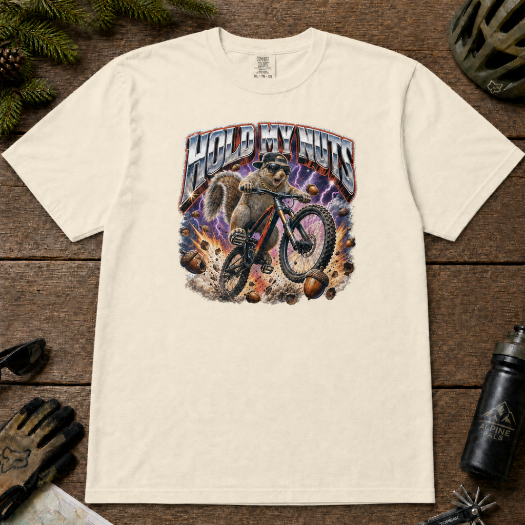 Ivory white t-shirt featuring a squirrel mountain biking through flying acorns beneath the words “Hold My Nuts.”