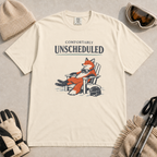 Ivory white t-shirt featuring a fox relaxing in a chair beside a ski helmet with the words “Comfortably Unscheduled.”