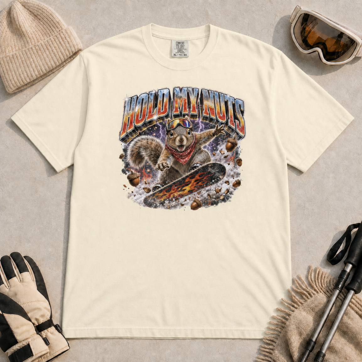 Ivory white t-shirt featuring a squirrel snowboarding through flying acorns beneath the words “Hold My Nuts.”
