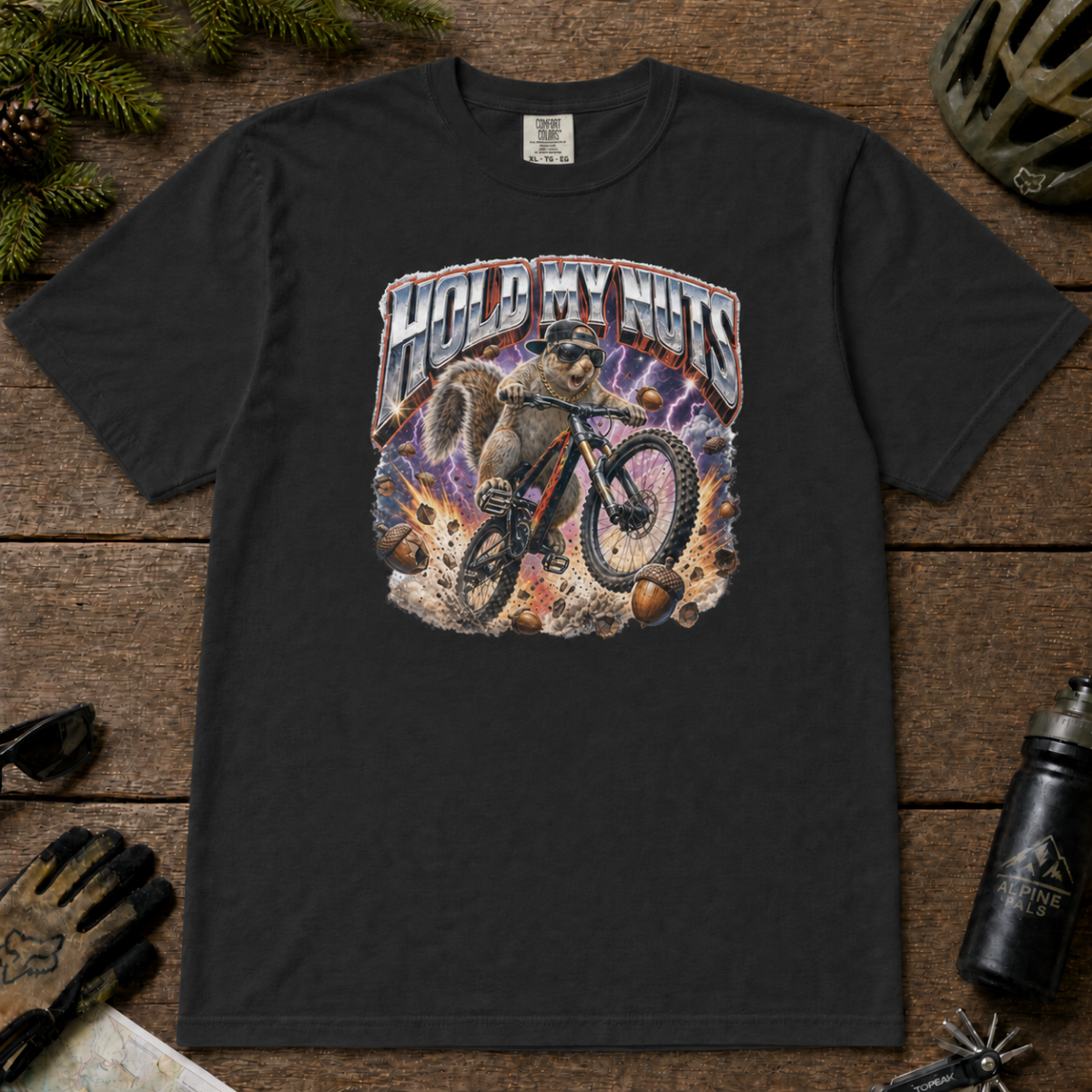 Black t-shirt featuring a squirrel mountain biking through flying acorns beneath the words “Hold My Nuts.”