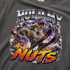 Close-up of a bold squirrel skiing design with purple lightning, flying acorns, and the words “Hold My Nuts” on a charcoal gray t-shirt.