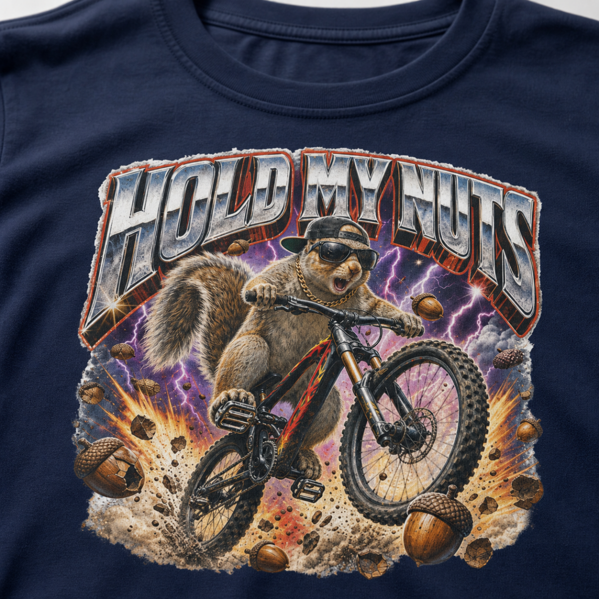Close-up of a bold squirrel mountain biking design with lightning, flying acorns, and the words “Hold My Nuts” on a charcoal navy blue t-shirt.