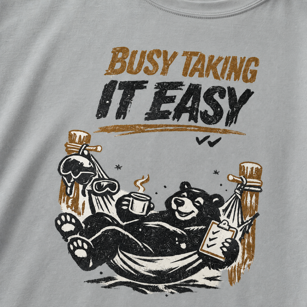 Close-up of a black bear relaxing in a ski-lodge hammock with a hot drink and checklist beneath the words “Busy Taking It Easy.”