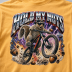 Close-up of a bold squirrel mountain biking design with lightning, flying acorns, and the words “Hold My Nuts” on a charcoal mustard yellow t-shirt.