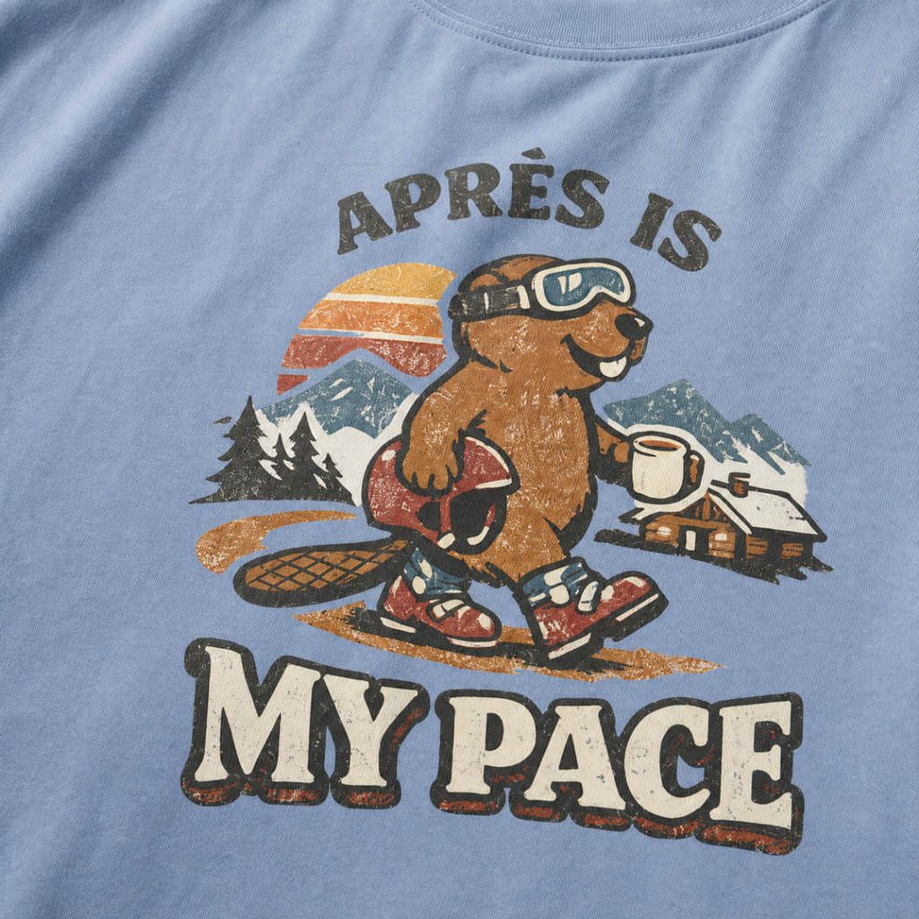 Close-up of a vintage beaver après-ski design with mountains, a cabin, and the words “Après Is My Pace” on a washed denim blue t-shirt.
