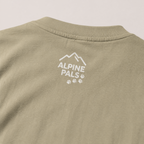 Close-up of a khaki colored shirt with 'Alpine Pals' logo on a beige background