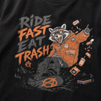 Black t-shirt with a graphic of a raccoon in an orange jacket and text 'Ride Fast Eat Trash' on a black background.