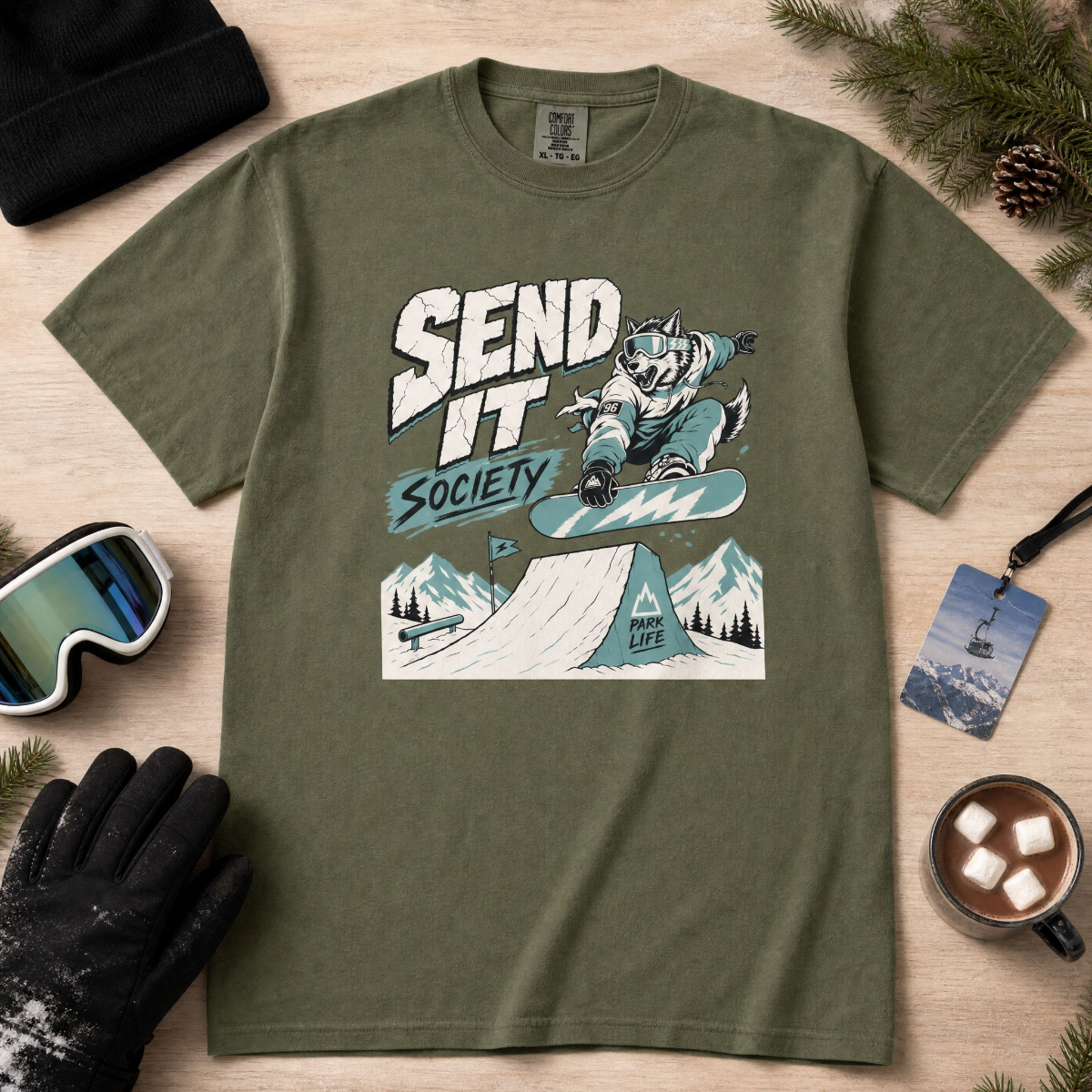Hemp green t-shirt with a graphic design of a person snowboarding, surrounded by winter accessories on a wooden surface.