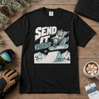 Black t-shirt with a graphic design of a snowboarder and text 'Send It Society' on a wooden surface with winter accessories.