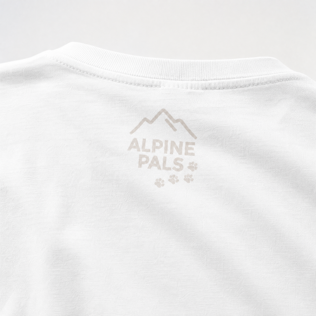 Close-up of a white shirt with 'Alpine Pals' logo on a light gray background