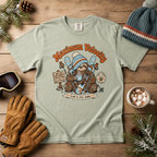 Light green t-shirt with a graphic design of a sloth with skis, surrounded by winter accessories on a wooden surface.