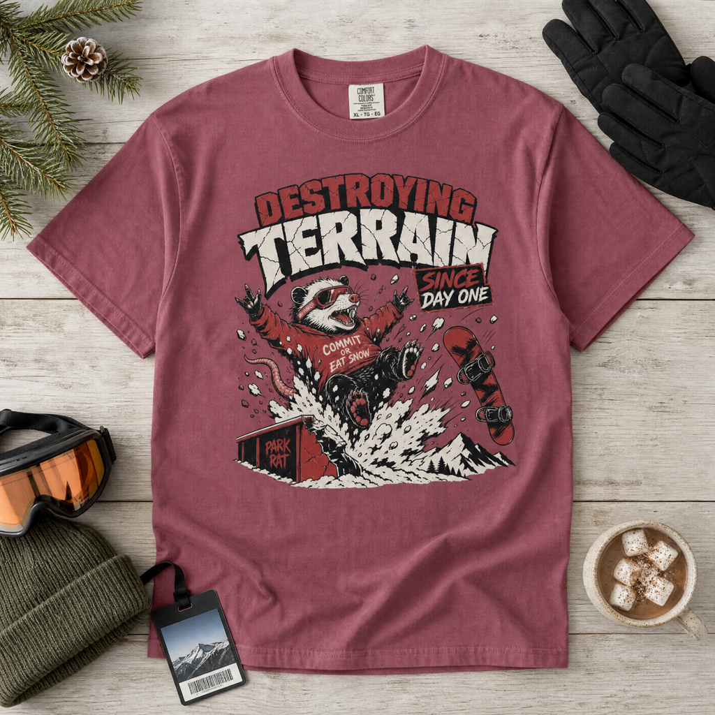 Brick red t-shirt with graphic design on a wooden surface with winter accessories.