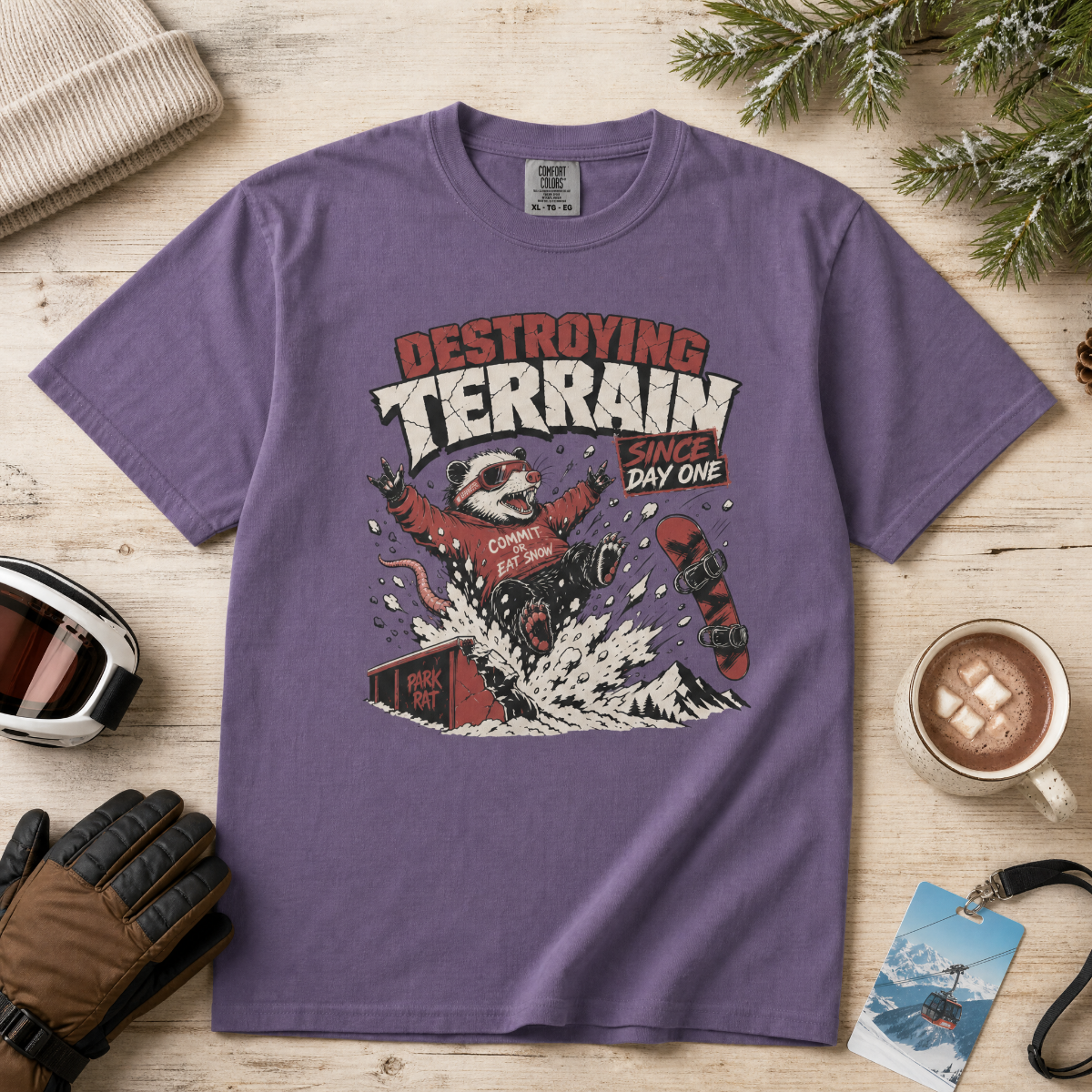 Grape purple t-shirt with graphic design on a wooden surface with winter accessories.