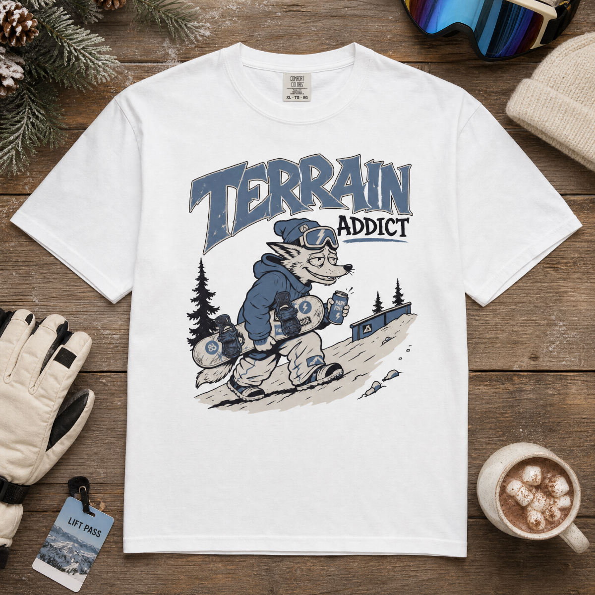 White t-shirt with 'Terrain Addict' graphic on a wooden surface with winter accessories.