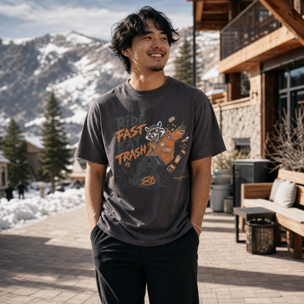 Man wearing a graphic t-shirt with text and design, standing outdoors with mountains in the background.