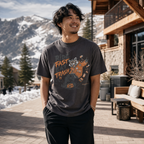 Man wearing a graphic t-shirt with text and design, standing outdoors with mountains in the background.