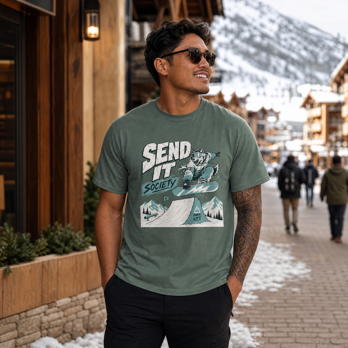 Man wearing a blue spruce green t-shirt with a graphic design in a snowy town setting