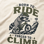 Ivory white t-shirt with a graphic of a raccoon riding a bike and text 'Born to Ride, Forced to Climb'.