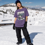 Person wearing a purple t-shirt with 'PARK' printed on it, standing in a snowy landscape with mountains in the background.
